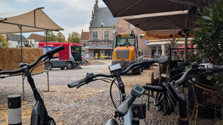Fietsen op de voorgrond op een terras, met schoonmaakwagen en wegwals op een historisch marktplein