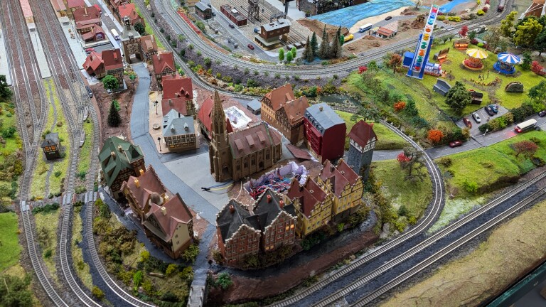 Miniatuurmodelspoor met dorpje rond kerk, meerdere spoorlijnen en kermis met attracties en reuzenrad