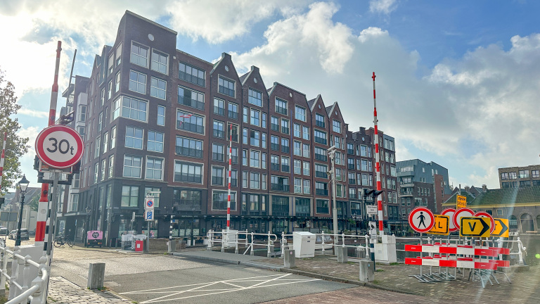 Groot modern bakstenen appartementencomplex aan een brug, met rood-witte slagbomen en verkeersborden (30t)