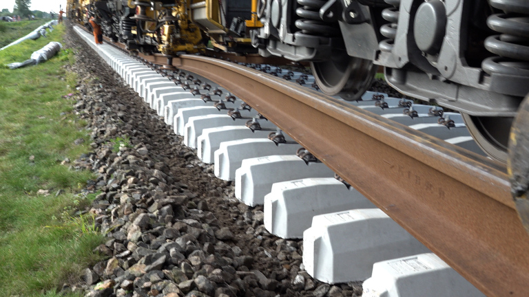 Detail van spoorrails met nieuwe betonnen dwarsliggers en wielen van een onderhoudstrein tijdens spoorwerkzaamheden