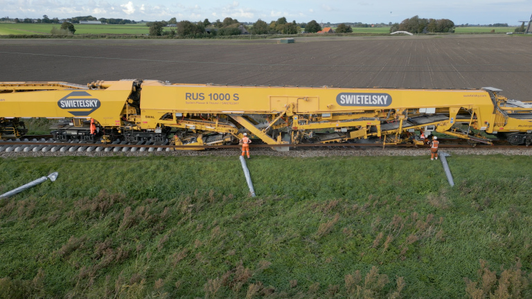 Gele Swietelsky RUS 1000 S spoorwerktrein met twee spoorwerkers langs een spoor in landelijk gebied