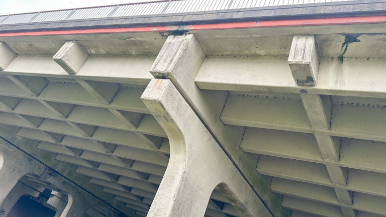 Onderzijde van een betonnen brug met ribbenstructuur en draagbalken, met donkere vocht- en roestvlekken langs de rand