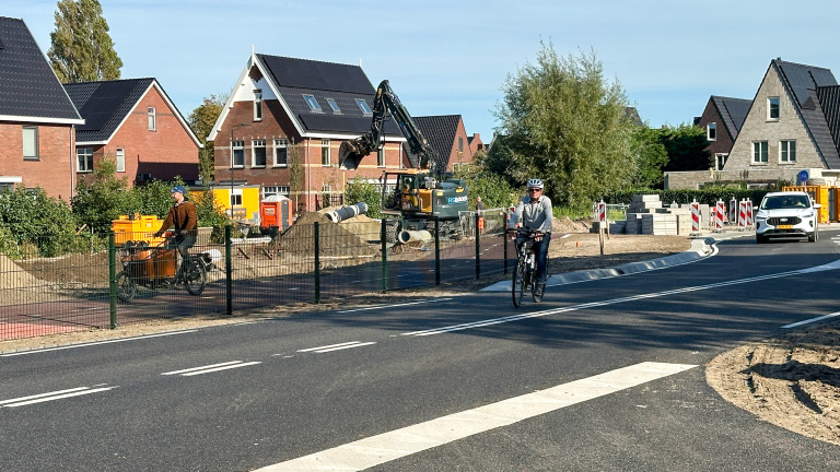 Fietser op de weg langs wegwerkzaamheden met graafmachine en afzettingen in een woonwijk