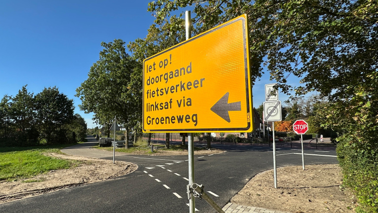 Geel omleidingsbord: “let op! doorgaand fietsverkeer linksaf via Groeneweg”, met pijl naar links bij kruispunt