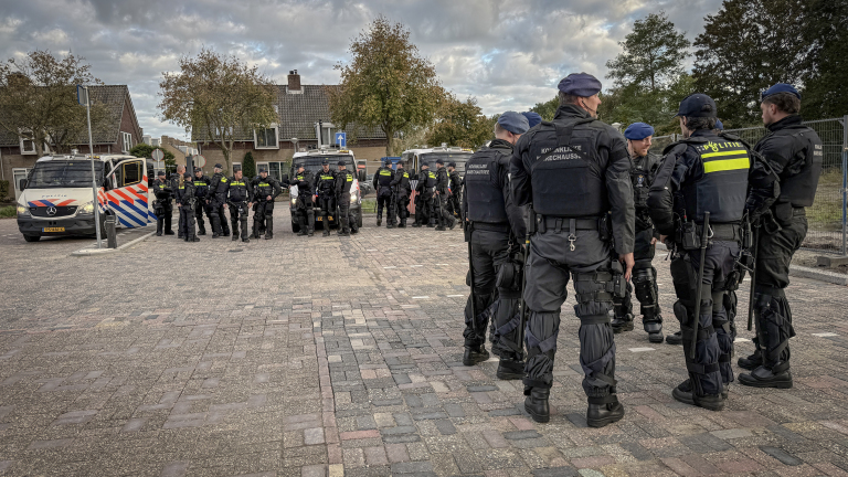 Groep politieagenten en marechaussees in oproeruitrusting bij politiebusjes in een woonwijk