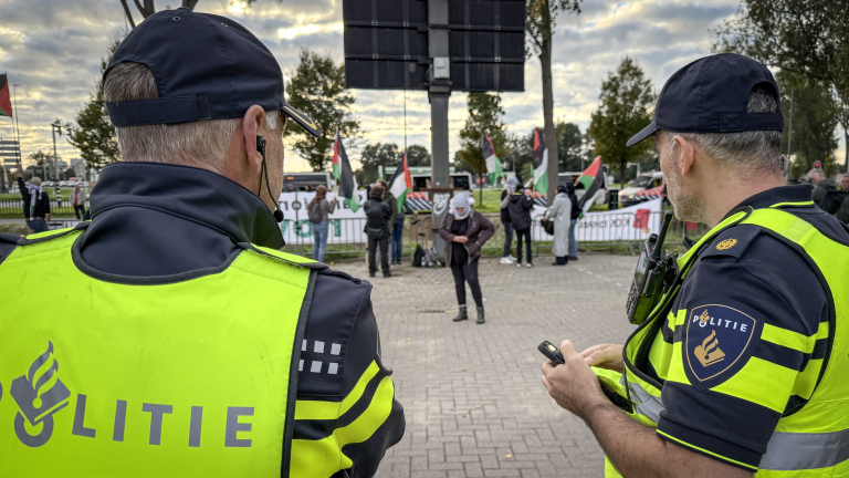 Twee politieagenten in gele hesjes kijken naar demonstranten met Palestijnse vlaggen achter dranghekken