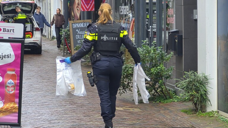 Politieagent draagt handschoenen en houdt twee zakken met bewijsmateriaal vast in een winkelstraat