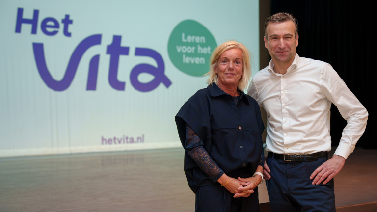 Twee mensen poseren voor een scherm met het logo Het Vita en de tekst Leren voor het leven