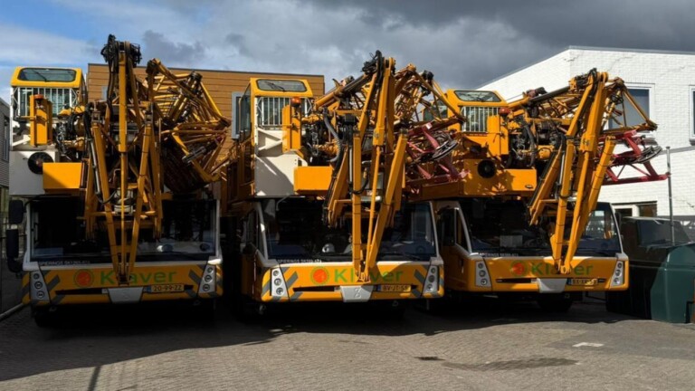 Drie gele hoogwerkers of kraanwagens staan naast elkaar geparkeerd op een industrieterrein