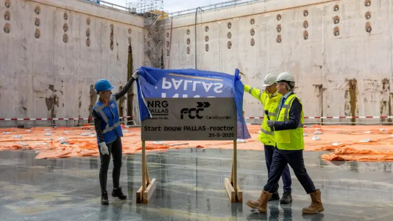 Drie bouwvakkers onthullen bord “Start bouw PALLAS-reactor 29-9-2025” in grote betonnen bouwkuip