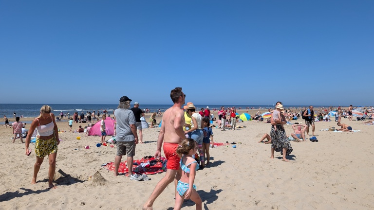 Mensen genieten van een zonnige dag op een druk strand met blauwe lucht en kalme zee.