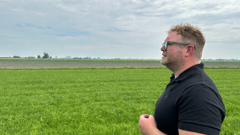 Een man in een zwarte polo staat in een groen veld en kijkt naar rechts.