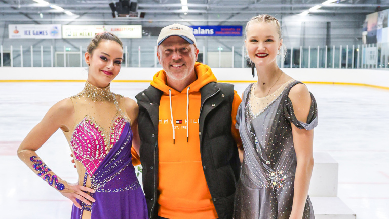 Twee kunstschaatsers poseren met een man in een ijsbaan.