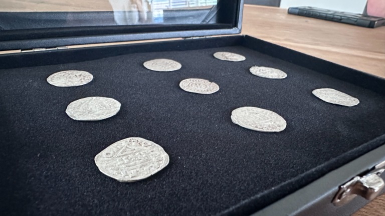 Een zwarte doos met negen oude munten op een fluwelen voering, geplaatst op een houten tafel.