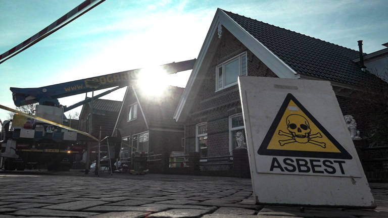 Een huis in renovatie met een asbestwaarschuwing en een hijskraan op de achtergrond.