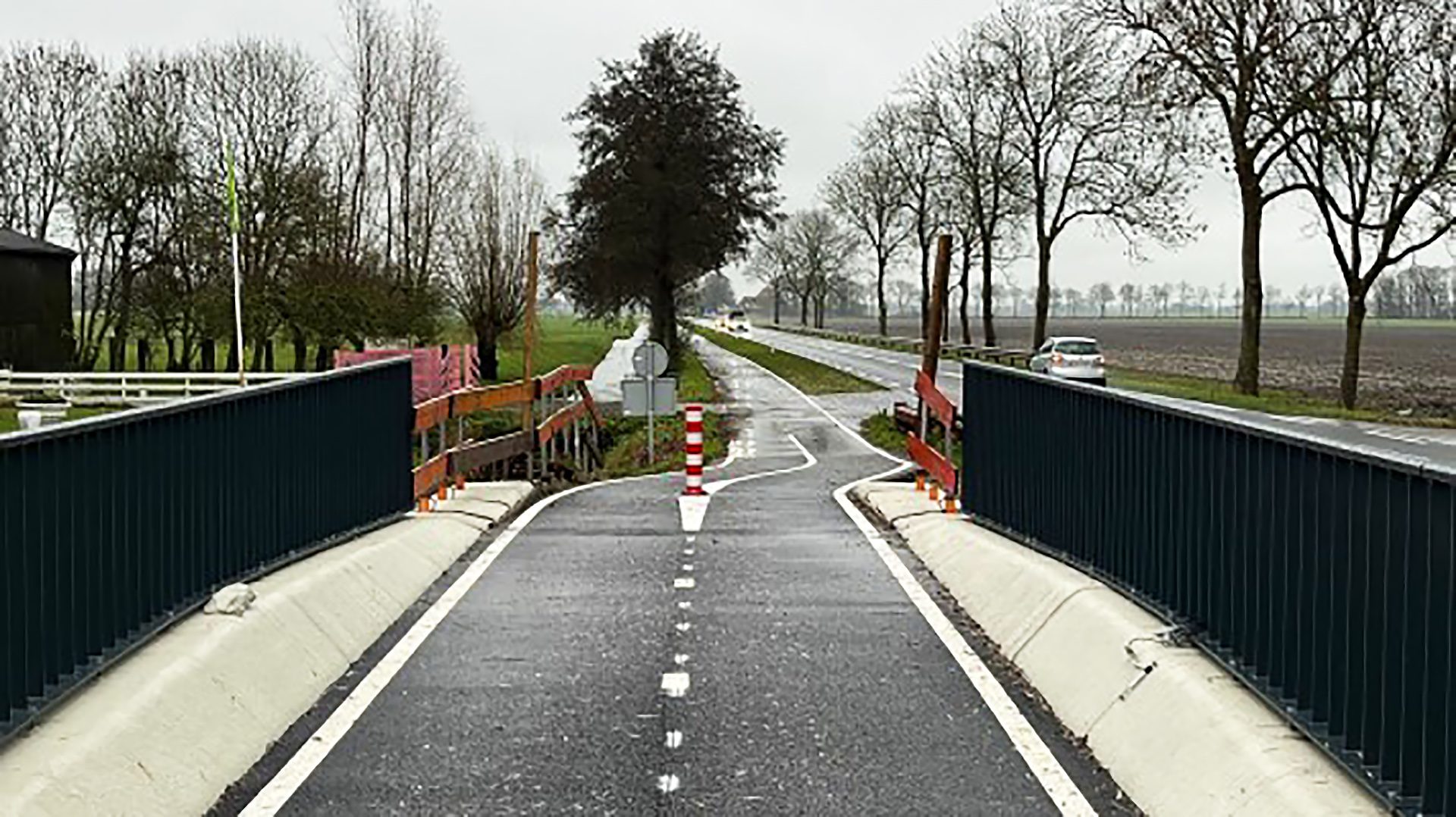 Fietspad dat een weg kruist met barriers aan weerszijden en een witte pijl op het asfalt.