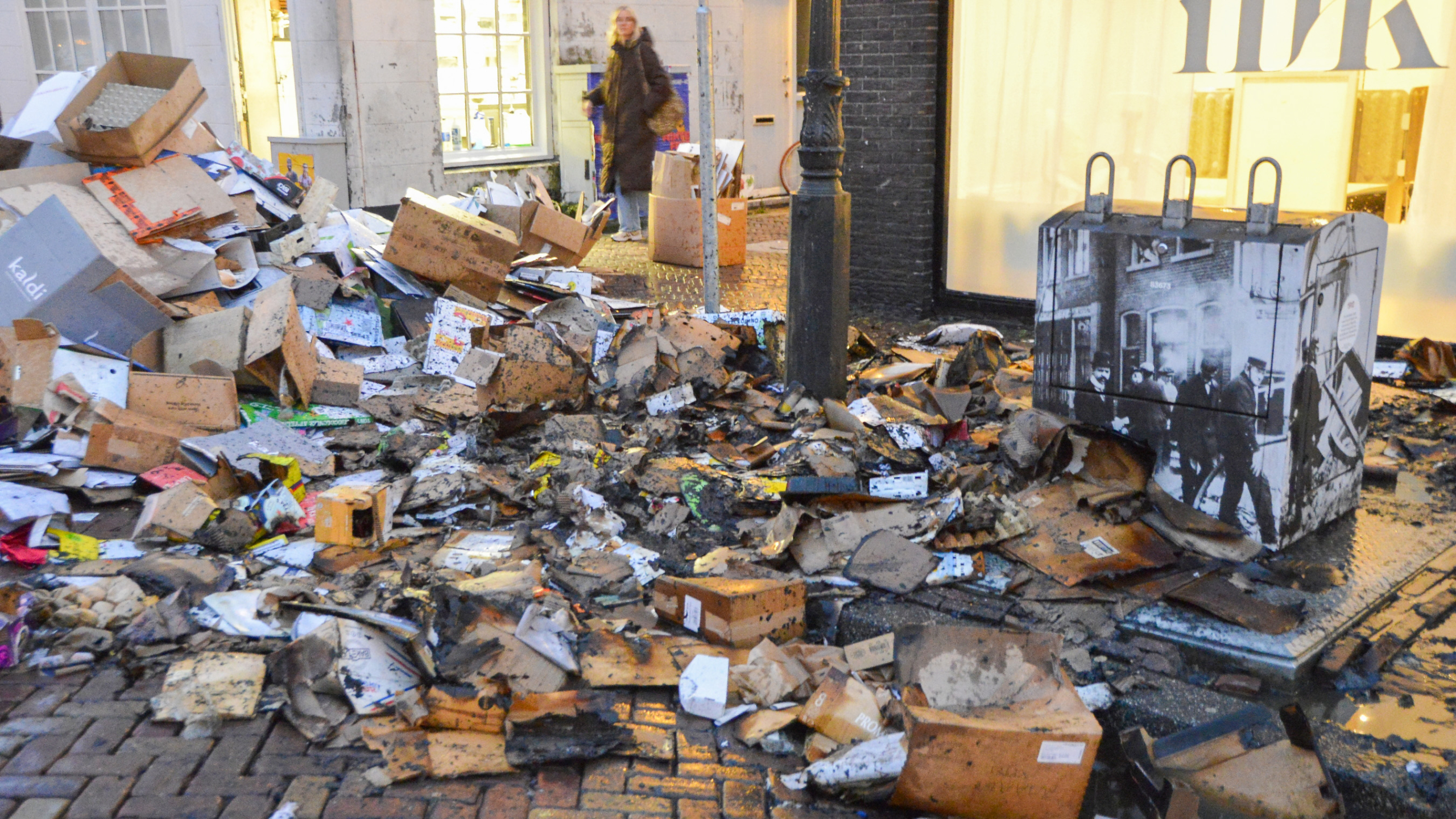 Afvalhopen van kartonnen dozen en puin op een natte straat naast een brandweerwagen en dicht bij een winkel.