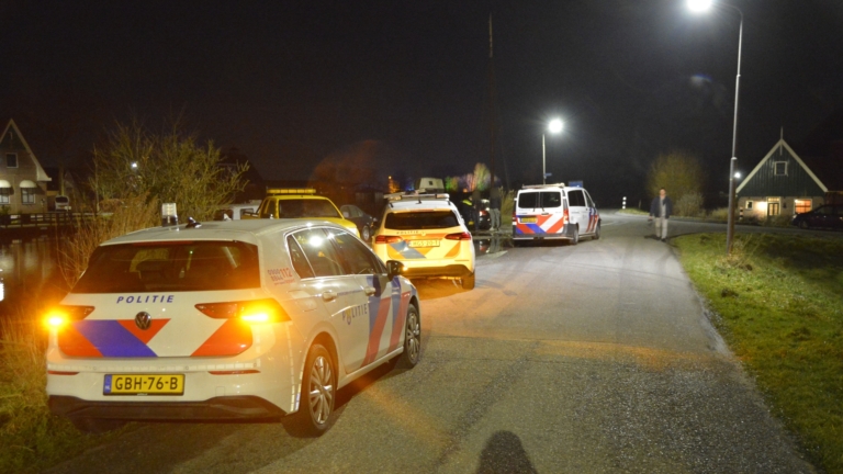 Meerdere politieauto's staan geparkeerd langs een weg in de nacht, met agenten bij een voertuig.