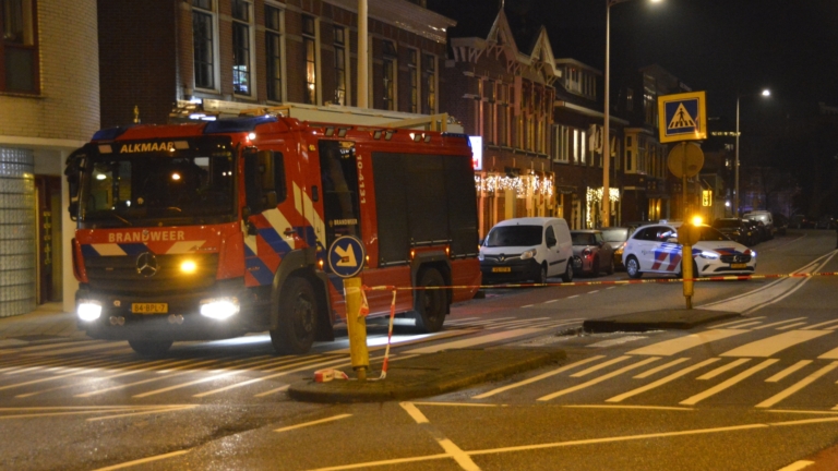 Een nachtelijke scène met een brandweerwagen en mensen, waaronder politie en een brandweerman, staande op een kruispunt.