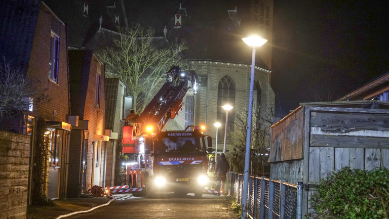 Brandweerauto met ladder in actie bij nacht naast een kerk, omgeven door woonhuizen.