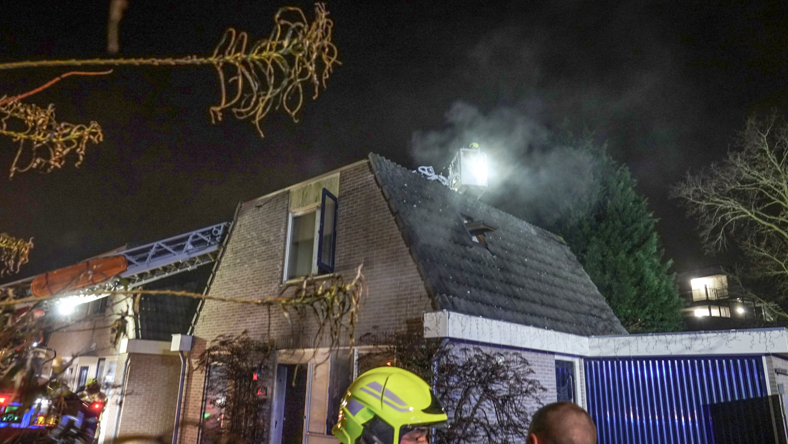 Brandweerauto met ladder in actie bij nacht naast een kerk, omgeven door woonhuizen.