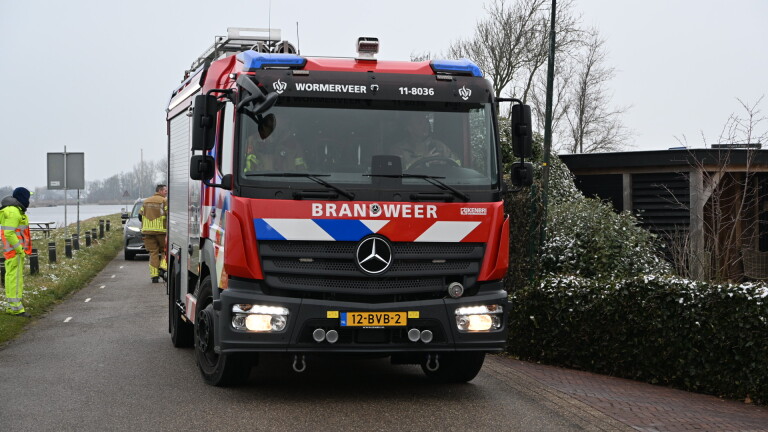 Wegwerkers in oranje en gele kleding graven een greppel langs een trottoir voor een huis.
