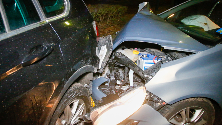 Auto-ongeluk in een woonwijk 's avonds, met twee voertuigen tegen elkaar, glas op de grond en politie-aanwezigheid.