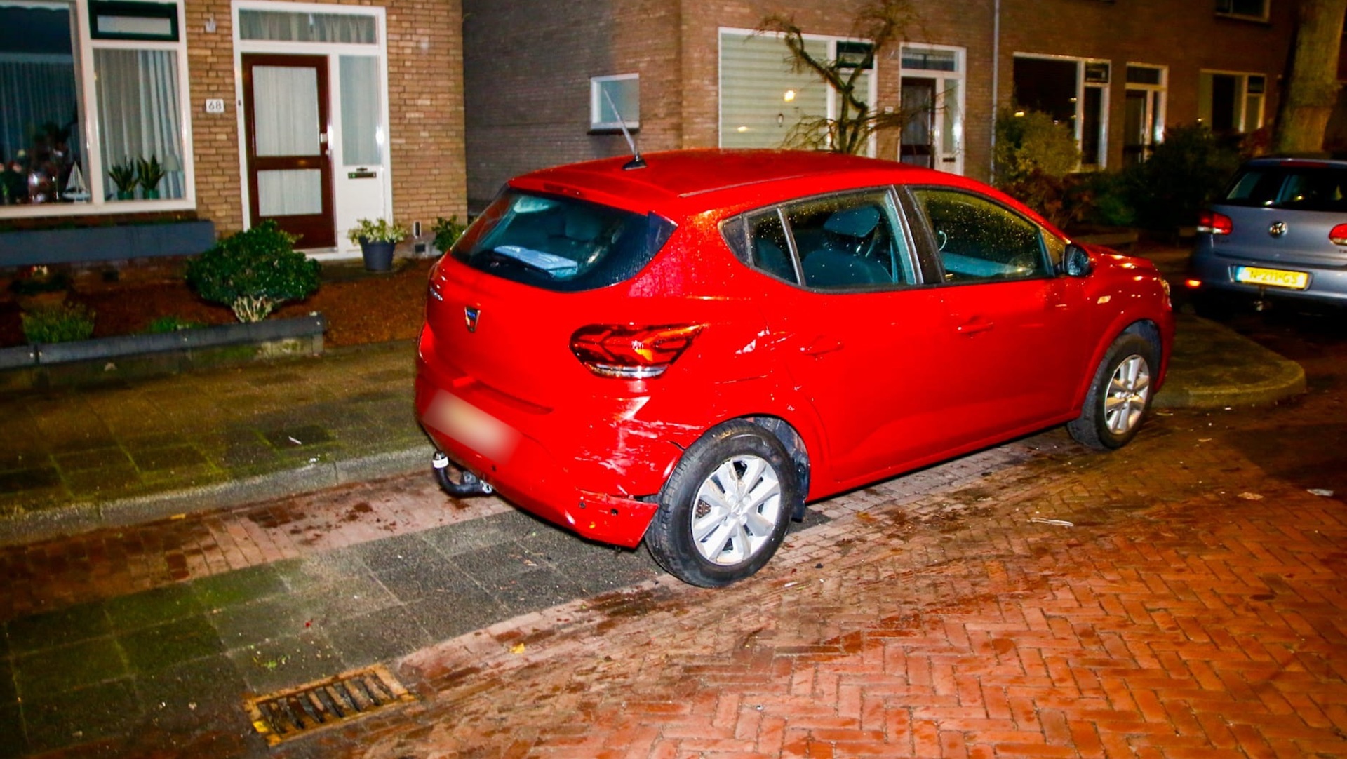 Beschadigde zwarte auto met krassen en deuken aan de voorkant, geparkeerd op een natte bakstenen weg.