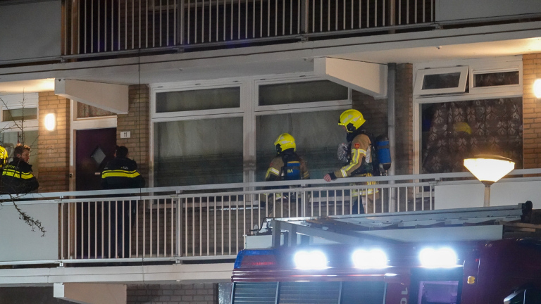 Brandweerwagens en brandweerlieden voor een flatgebouw, 's nachts. Mensen zijn buiten en omstanders kijken toe.
