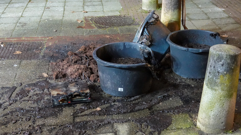 Brandweerwagens en brandweerlieden voor een flatgebouw, 's nachts. Mensen zijn buiten en omstanders kijken toe.