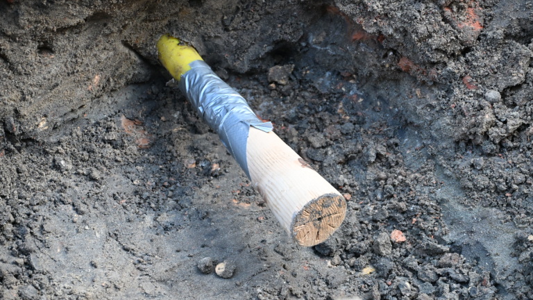 Straat met wegwerkzaamheden, een arbeider in felgeel pak en een graafmachine, omgeven door oranje hekken.