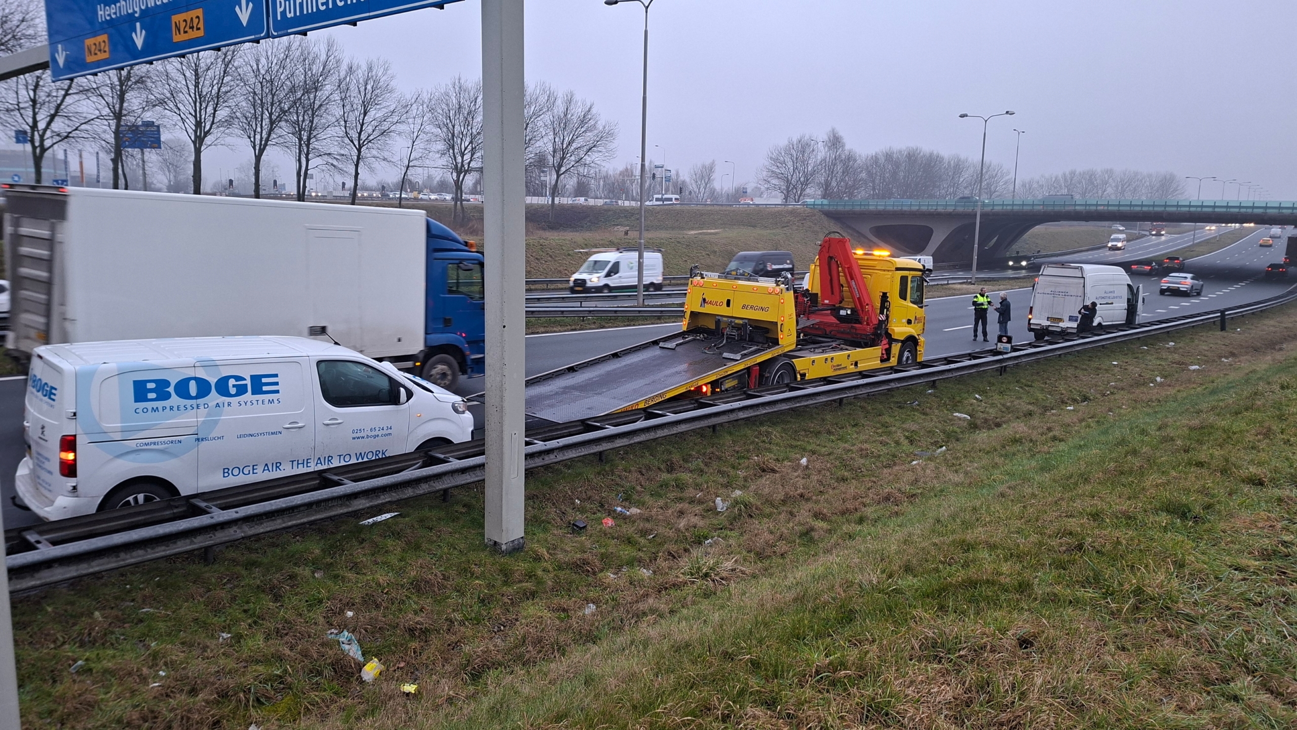 Een witte bestelwagen met zware schade aan de voorkant staat langs de weg na een ongeval.