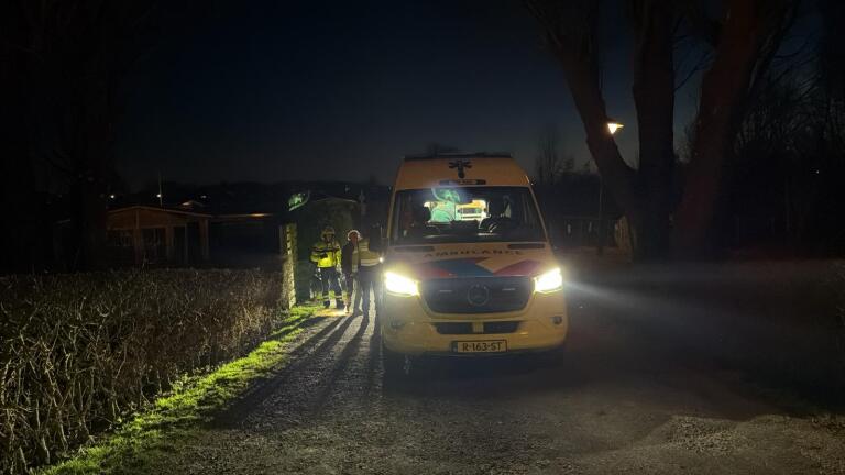 Ambulancepersoneel en politie zijn 's nachts bezig bij een draaiende ambulance, met een paar mensen op de grond.