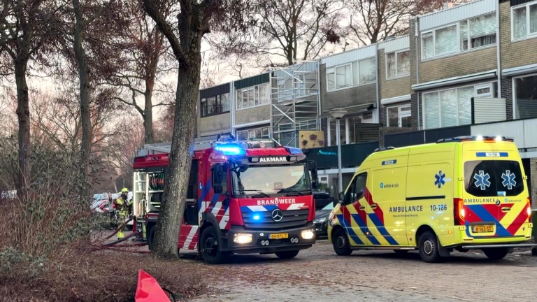 Brandweerauto's staan voor een huis waar dikke rookpluimen uit de ramen komen; een politieagent is aanwezig.
