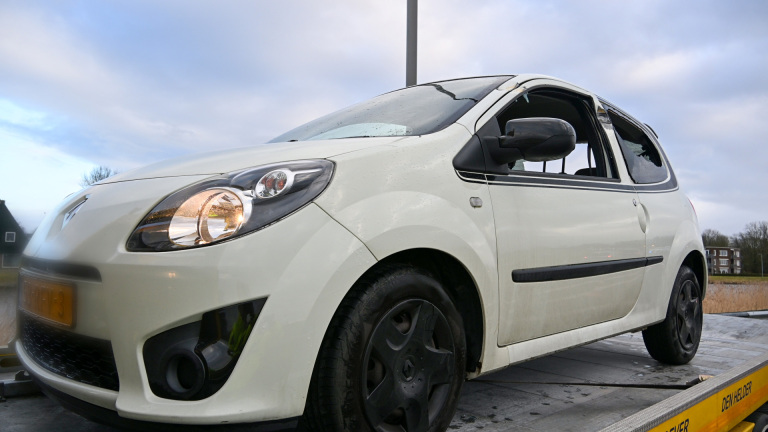 Rode vrachtwagen van Lubbers met lange oplegger en container, geparkeerd langs een weg met gebouwen en een molen op de achtergrond.