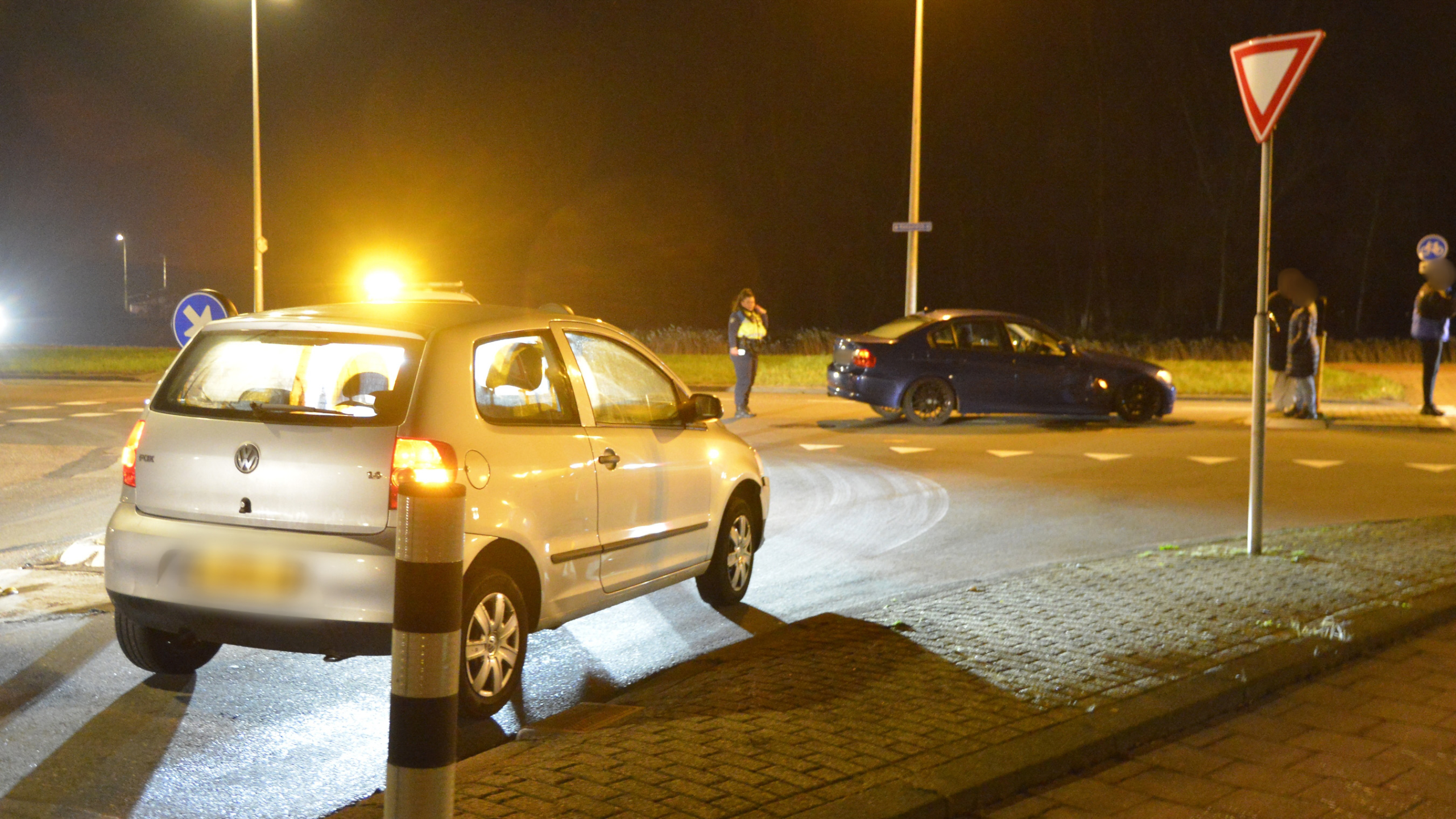 Auto-ongeluk bij nacht op kruispunt, met schade aan twee voertuigen; man in veiligheidskleding onderzoekt de situatie.