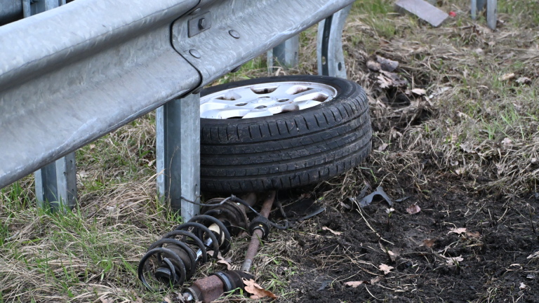 Auto met schade aan de voorzijde naast een vangrail op de snelweg, met een gele sleepwagen op de achtergrond.