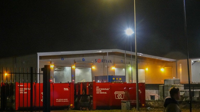 Industriepand van Sortiva bij nacht, met rode containers ervoor en verlichting die het terrein verlicht.