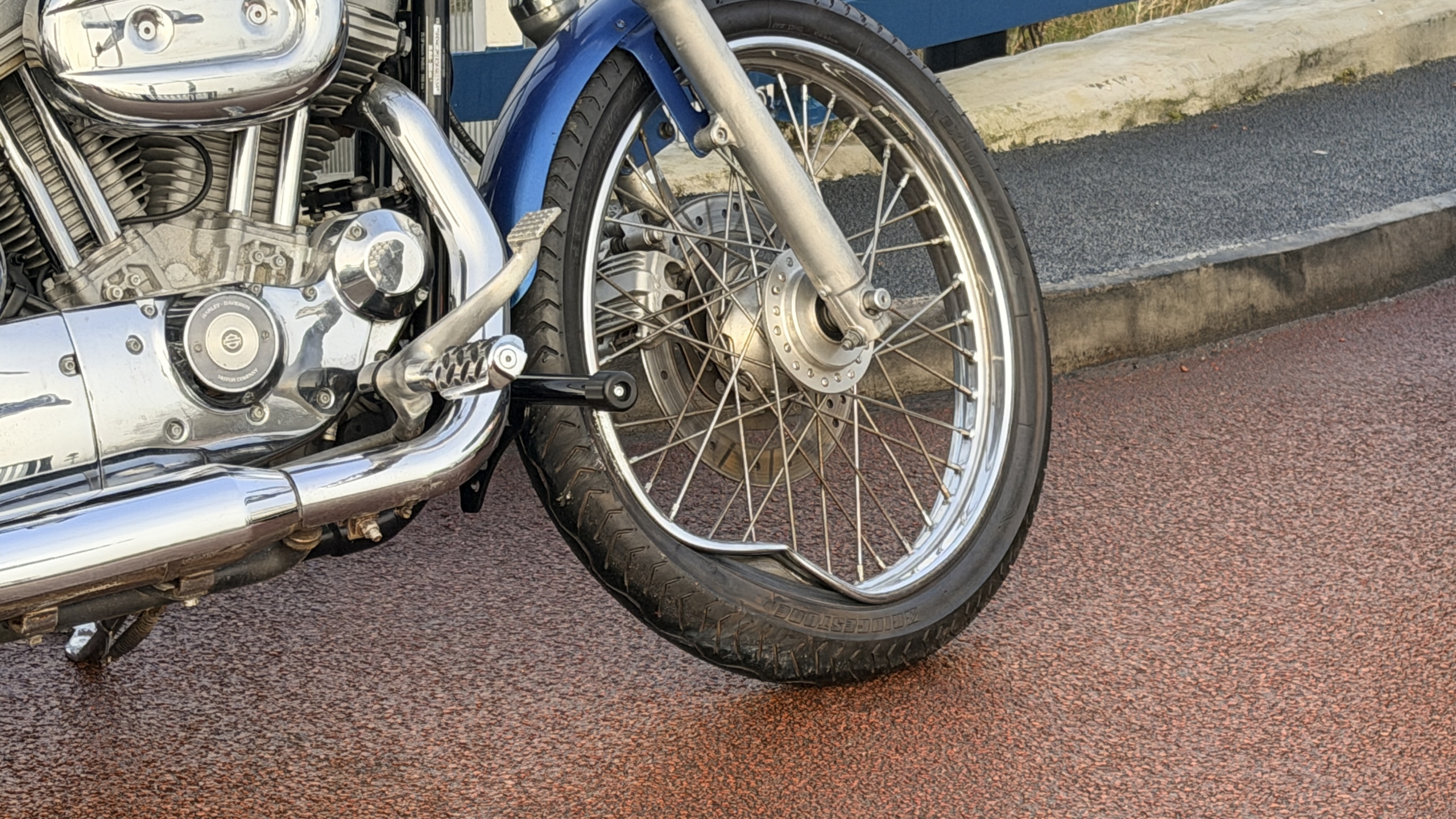 Een politieagent in geel uniform spreekt een man aan naast een geparkeerde motorfiets, met een auto op de achtergrond.