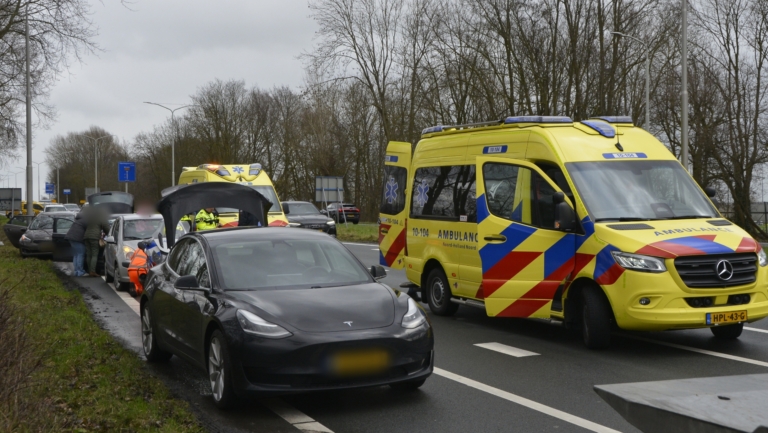 Auto-ongeluk met meerdere voertuigen langs een weg; ambulancepersoneel is aanwezig, en er staat een ambulance geparkeerd.