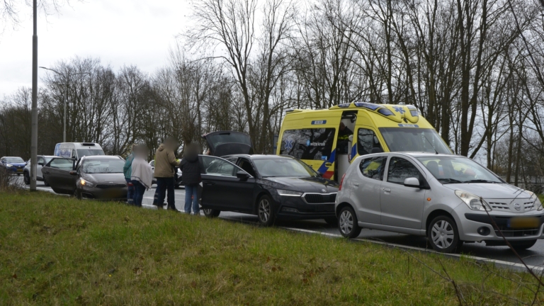 Auto-ongeluk met meerdere voertuigen langs een weg; ambulancepersoneel is aanwezig, en er staat een ambulance geparkeerd.