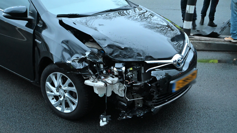 Verkeersongeval op kruispunt met politieauto en meerdere betrokken auto's op een regenachtige dag.