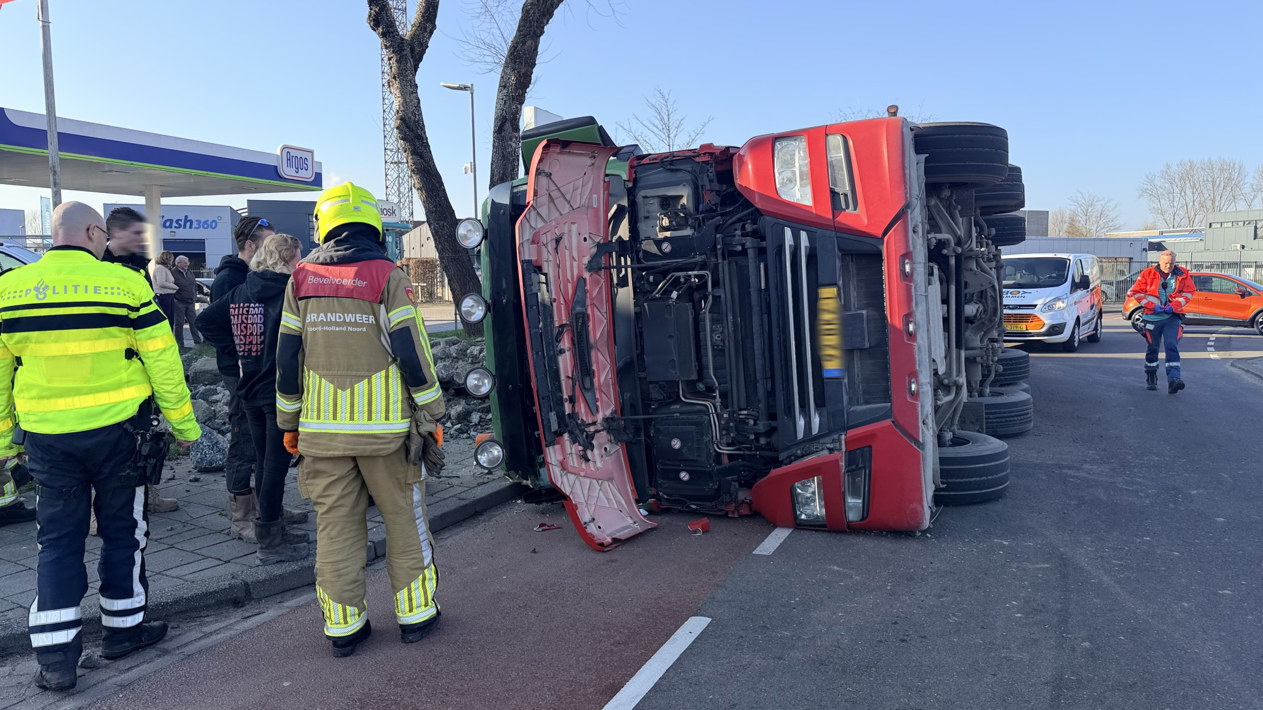 Een gekantelde vrachtwagen met verspreide stenen, omringd door hulpverleners in uniformen en voertuigen met zwaailichten.