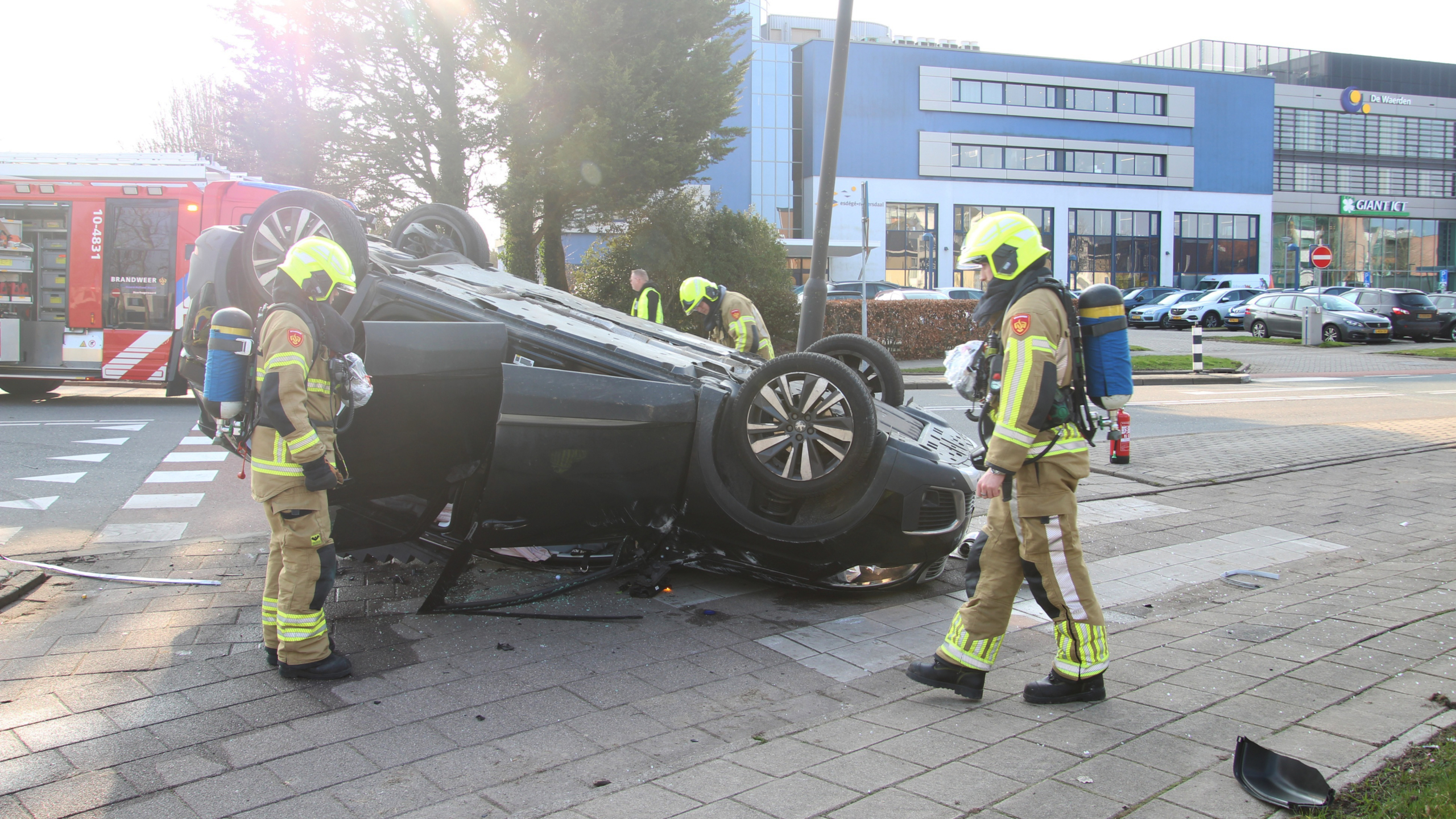Auto ligt ondersteboven op straat na ongeval, omringd door hulpverleners, met een brandblusser op de voorgrond.