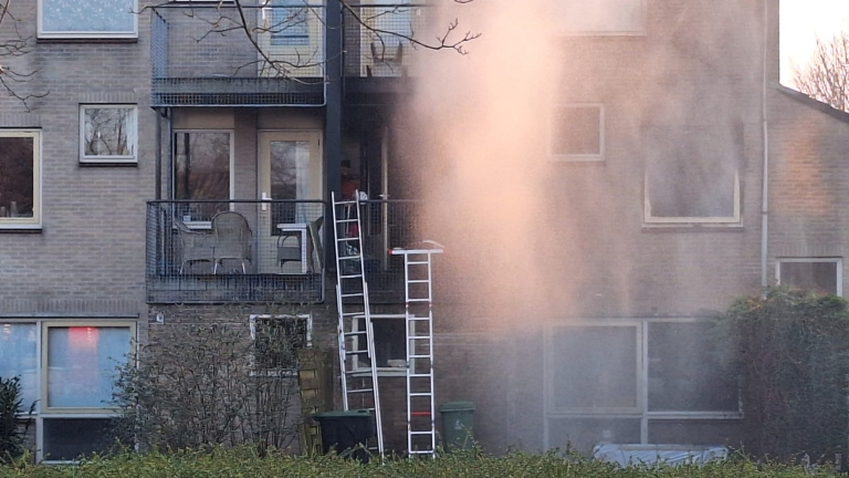 Brandweerwagen bij appartementencomplex met afzetlint en waterschade zichtbaar op gevel.