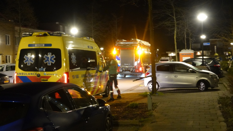 Brandweerlieden in actie bij een appartementengebouw met een brandweerwagen op de voorgrond en auto's op de parkeerplaats.