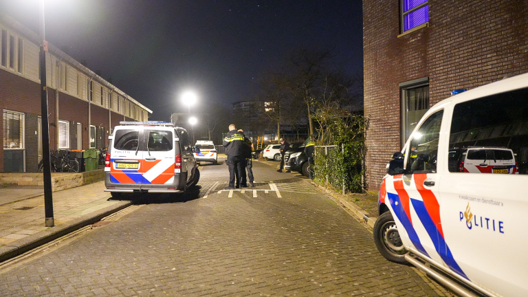 Politieauto's geparkeerd op een straat 's nachts, met meerdere mensen die naast een voertuig staan praten.