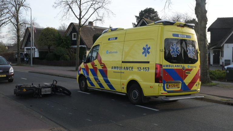 Politieagenten en een ambulance bij een verkeersongeval met een omgevallen scooter op de weg, naast een geparkeerde auto.
