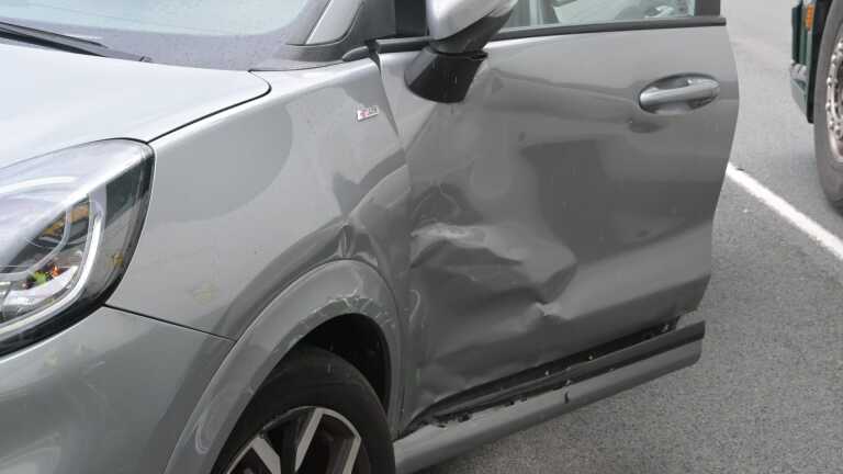 Een vrachtwagen, auto en ambulance staan stil bij een verkeerslicht. Mensen staan naast de voertuigen in gesprek.