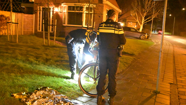 Politieagenten controleren 's nachts een fiets op een troittoir; een man kijkt toe.